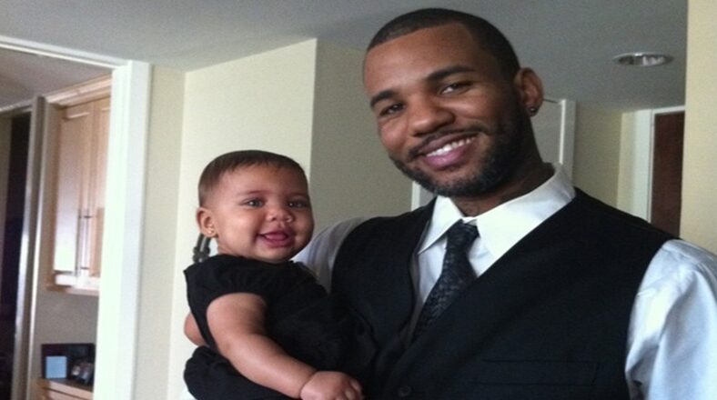 Game holding his daughter, both dressed in black, after his grandfather's funeral, smiling despite the emotional day.