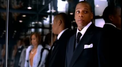 Jay-Z in a scene from the Excuse Me Miss music video, dressed in a black suit in an elegant setting, capturing the song’s smooth, luxurious vibe.
