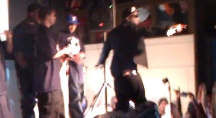Young Jeezy performing on stage during a live concert, interacting with the audience while surrounded by his crew.