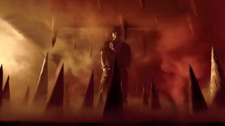 Young Jeezy in a fiery, dramatic scene from the 'Ballin' music video, surrounded by sharp spikes and intense lighting