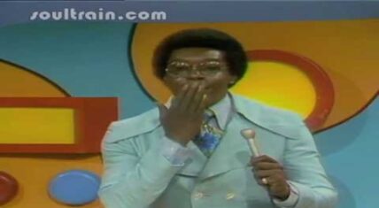 Don Cornelius, creator of Soul Train, standing in front of a Soul Train logo
