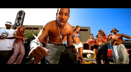 Ludacris performing shirtless in the "What's Your Fantasy" music video, surrounded by dancers and a vibrant party atmosphere.