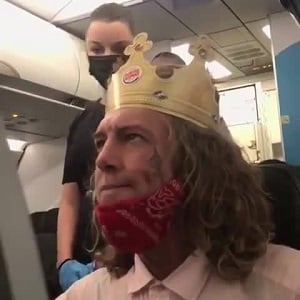 A white man, on an airplane, wearing a Burger King crown, was screaming racial slurs. The man kept screaming "n*gger b*tch," and repeatedly said "n*gger." When the flight attendant asked him to calm down, the man accused the woman of putting her stuff in his seat, and then accused her of kneeing him in the stomach.