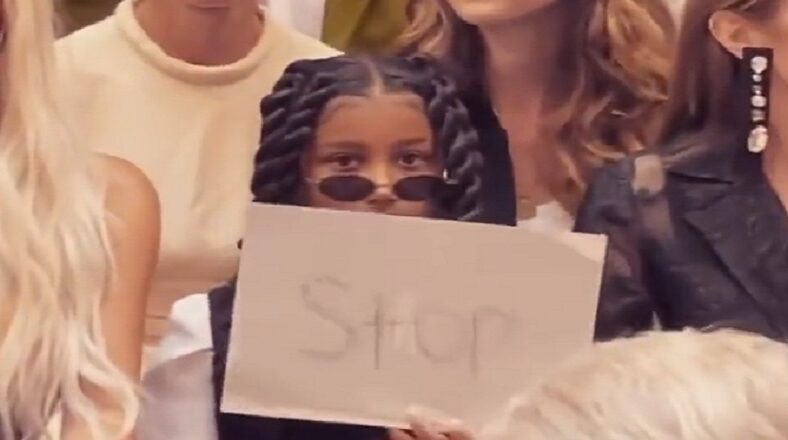 North West holds up sign that reads STOP to people taking pictures of her