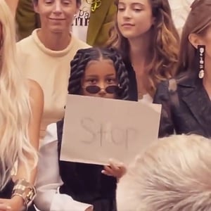 North West holds up sign that reads STOP to people taking pictures of her