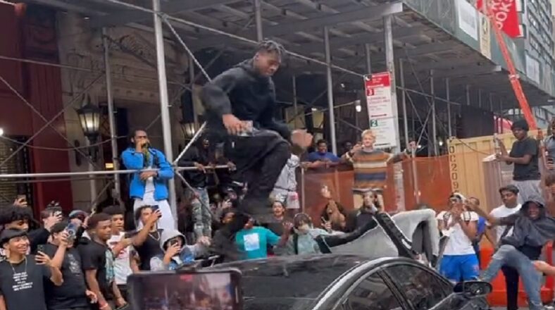People in NYC destroy a car as one man dances on top of it