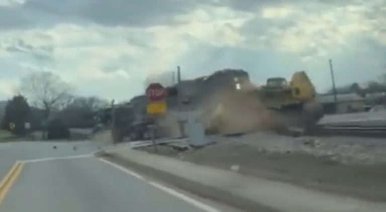 Truck carrying bulldozer gets stuck on train tracks as train comes