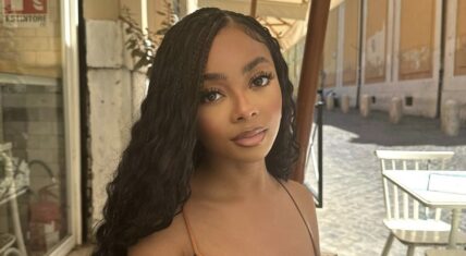 Skai Jackson sitting outdoors in a casual setting, with long, curly hair and a neutral-toned outfit, looking directly at the camera with a calm expression.