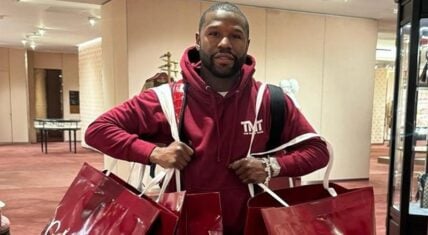 Floyd Mayweather holding luxury shopping bags, wearing TMT-branded clothing, showcasing his opulent lifestyle.