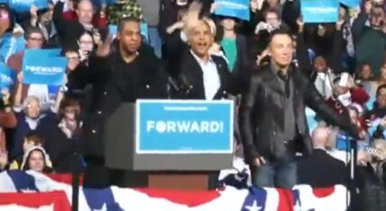 Jay-Z stands with President Barack Obama at a 2012 re-election rally in Ohio. The pair appear onstage before a crowd waving "FORWARD!" signs.