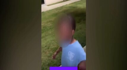 Blurred image of a young child wearing a light blue t-shirt standing on grass outdoors near a building, captured from footage of the 5-year-old boy found wandering alone at night in Greenville, North Carolina.