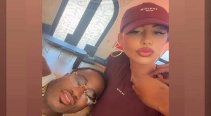 Amber Rose and Adrien Broner in a close-up selfie, with Broner leaning his head on her shoulder wearing gold chains and sunglasses while Rose wears a maroon 