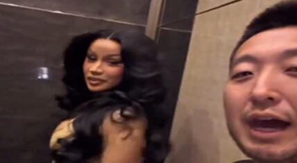 Cardi B stands in an elevator beside Kevin Wong, who is filming a selfie-style clip while asking her for dating advice on how to date a baddie.