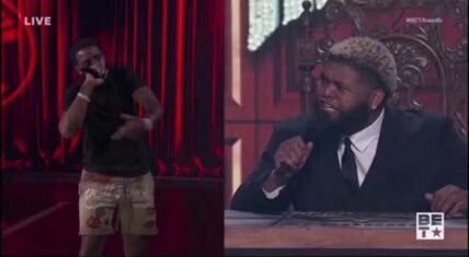 Split-screen from Druski's Coulda Been Records audition at the 2026 BET Awards: a performer in black t-shirt and sequined shorts raps energetically into a microphone on stage (left), while the suited executive with blonde curly hair reacts while holding a mic at the desk (right). LIVE #BETAwards broadcast.