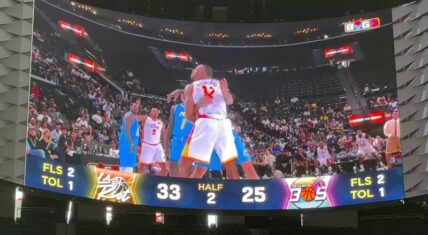 Arena Jumbotron displays a physical confrontation during a BIG3 basketball game between LA Riot and Miami 3's, showing Dwight Howard (#12, white jersey) engaged with opposing players in blue jerseys as officials intervene, with scorebug reading 33-25 in the second half.