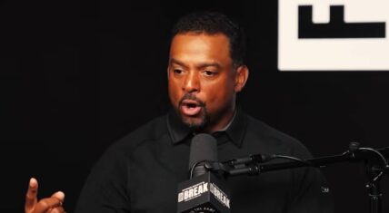 Alfonso Ribeiro speaking and gesturing with his right hand during an appearance on Byron Scott's Fast Break podcast, wearing a black polo shirt with a microphone in front.
