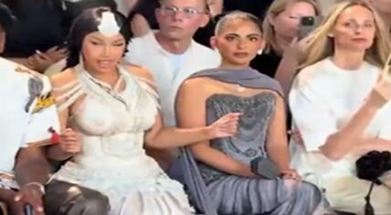 Cardi B in a white beaded gown with headpiece seated front row at Rahul Mishra's Paris Haute Couture show, reacting animatedly to the music beside Isha Ambani in a grey draped gown.