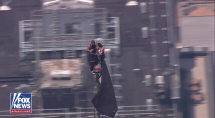 Two people standing atop the Empire State Building's 1,454-foot spire unfurl a large black banner reading 