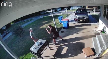 Ring doorbell camera still of a UPS driver in brown uniform confronting an angry homeowner in a suburban driveway, with a cardboard box on the ground and a dark Ford pickup truck parked nearby.