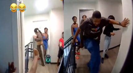 Ring camera screenshot of a chaotic apartment hallway at door 12, showing a heavyset man in a PlayStation t-shirt lunging aggressively with arms extended while a group of women in casual clothing stand nearby on the landing, with laughing emojis overlaid.